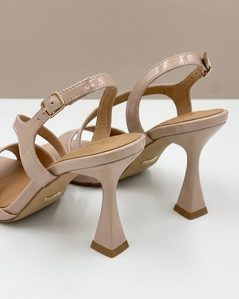 Sandalo da donna elegante in finitura nude/cipria lucido, con listino sottile incrociato sul collo del piede, punta squadrata moderna e tacco a rocchetto-retro.