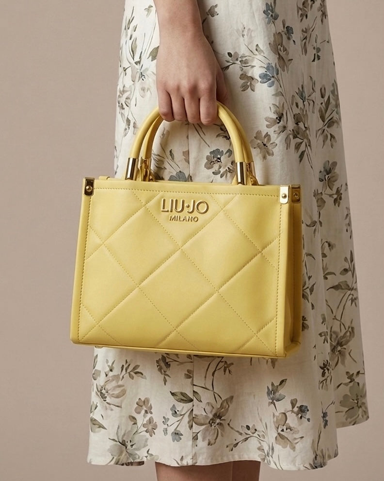 Borsa a mano Liu Jo color giallo sole con lavorazione trapuntata geometrica, logo frontale dorato "LIU·JO MILANO" e doppi manici rigidi-modella.