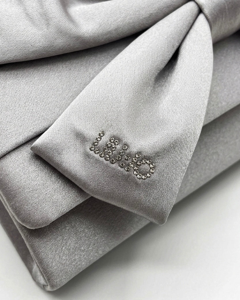 Borsa clutch Liu Jo in raso grigio argento con maxi fiocco frontale, logo in strass e tracolla a catena oro-logo.