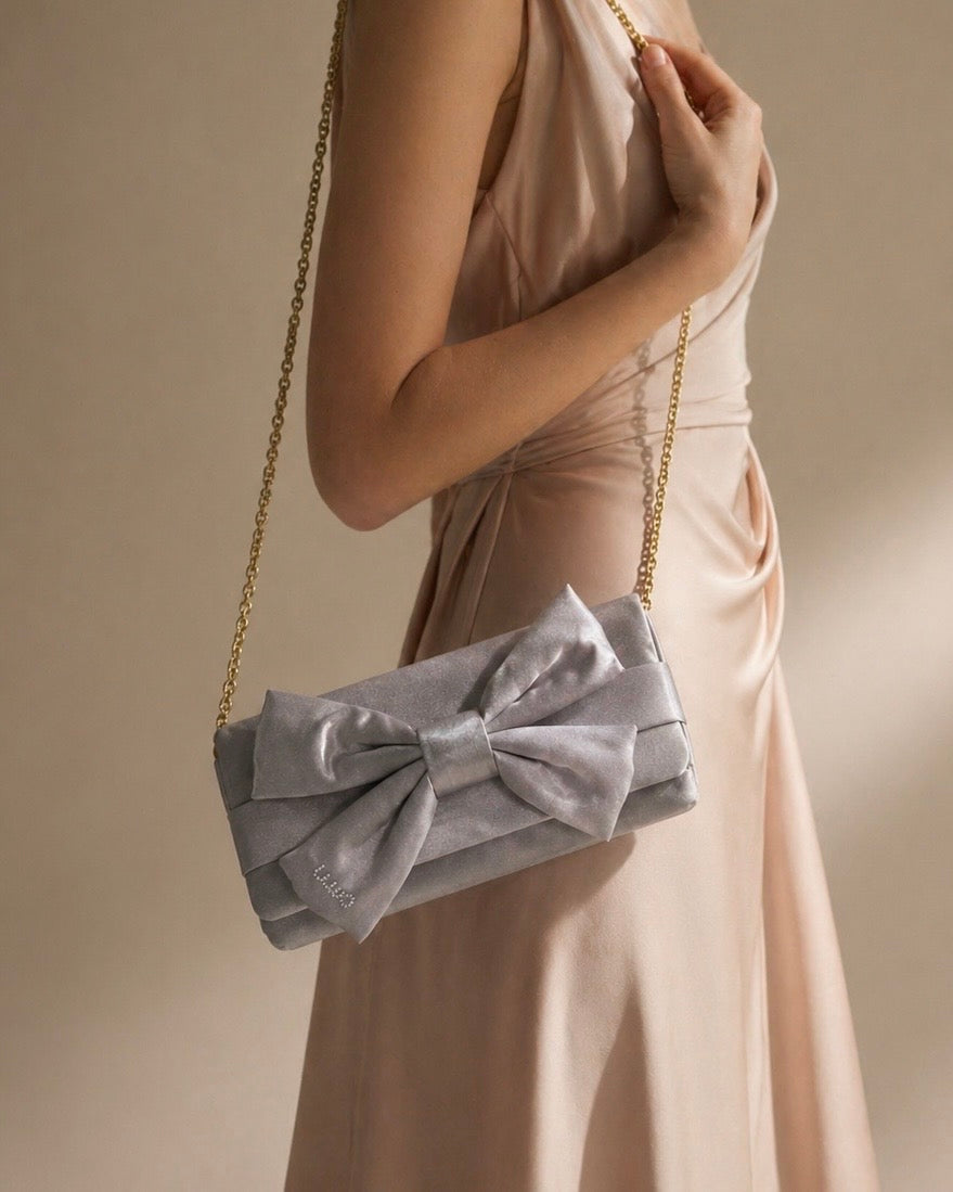Borsa clutch Liu Jo in raso grigio argento con maxi fiocco frontale, logo in strass e tracolla a catena oro-modella.