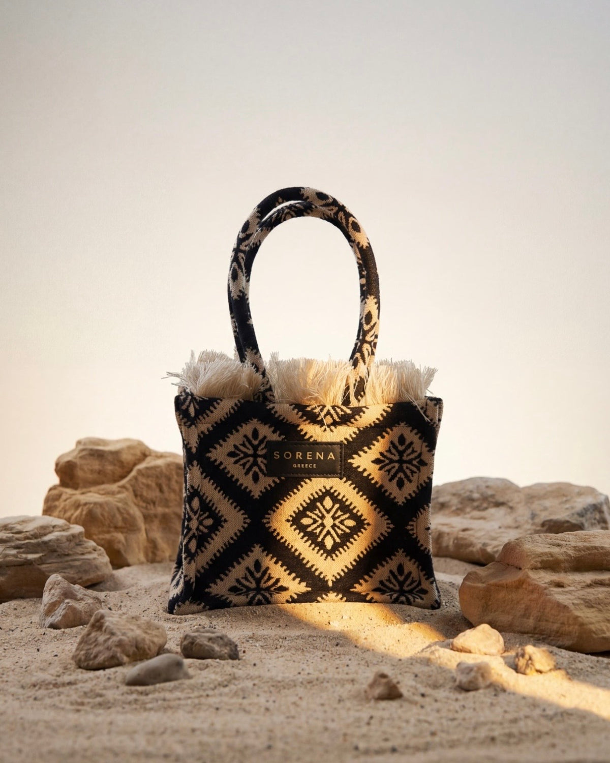Borsa a mano Sorena prodotta in Grecia in tessuto jacquard geometrico nero e beige con frange dorate e manici in tinta - Buttò Calzature.