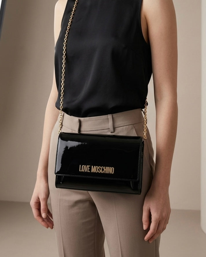 Borse Love Moschino in vernice nera lucida con tracolla a catena e logo dorato frontale-modella.