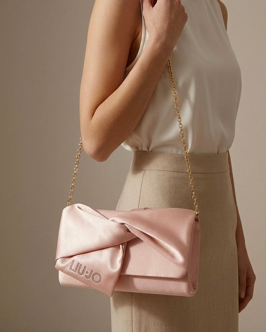 Pochette Liu Jo in satin rosa cipria con nodo centrale e logo in strass e catenina oro-modella.