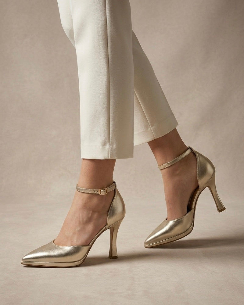 Scarpe décolleté eleganti color oro laminato, punta affusolata, tacco alto a rocchetto e cinturino sottile regolabile alla caviglia-indossate.