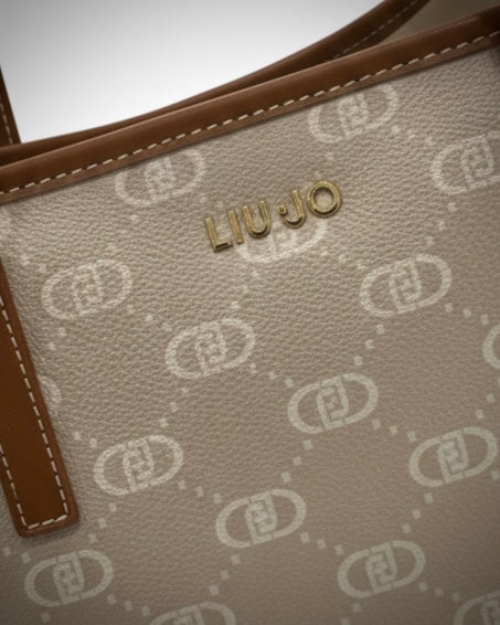 Dettaglio ravvicinato del logo metallico dorato Liu Jo su borsa monogram beige.