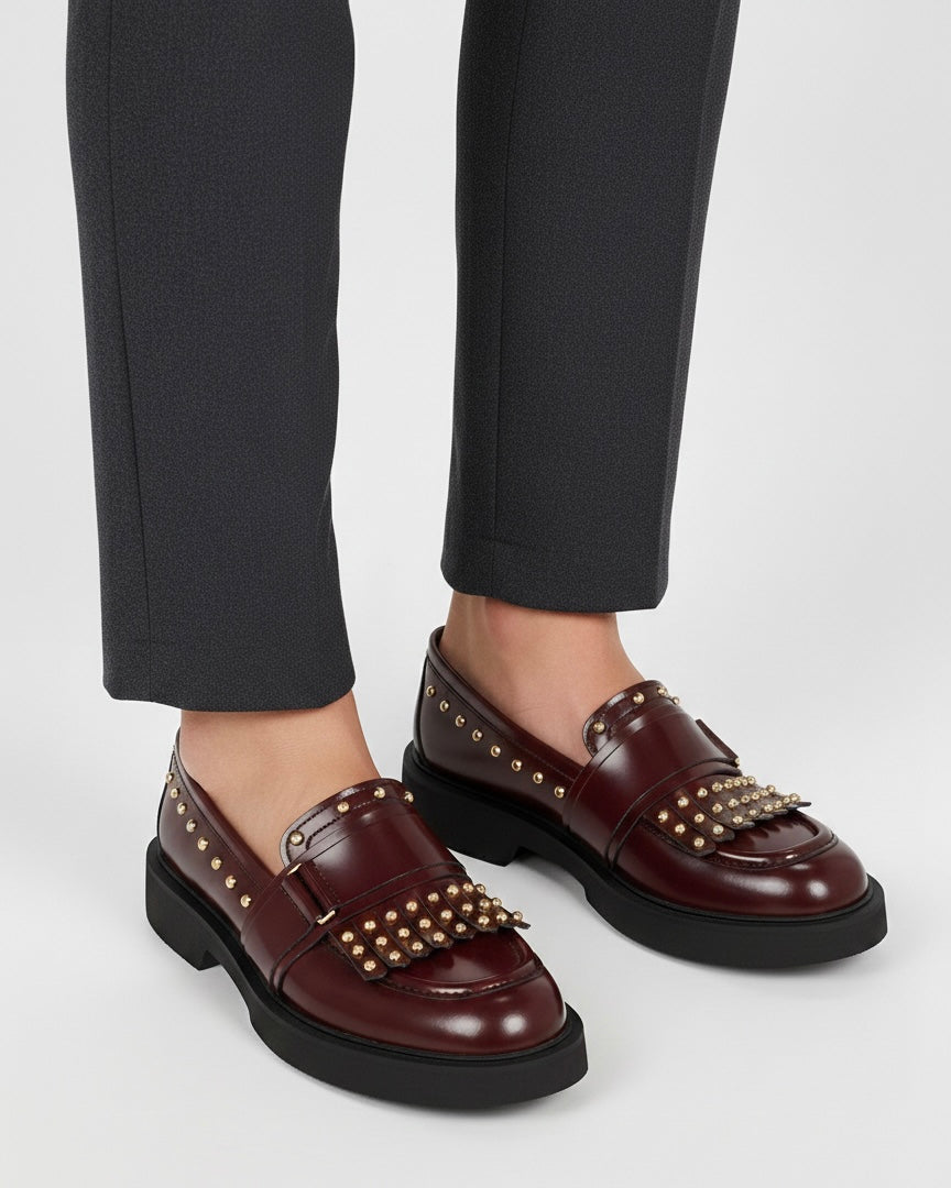 Mocassini bordeaux in pelle lucida con frange, borchie dorate decorative e suola platform nera spessa - indossati.
