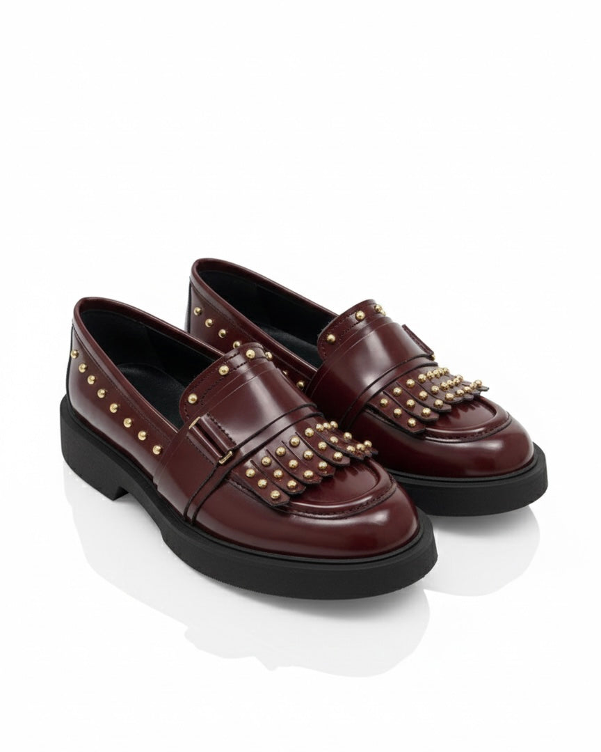 Mocassini bordeaux in pelle lucida con frange, borchie dorate decorative e suola platform nera spessa.