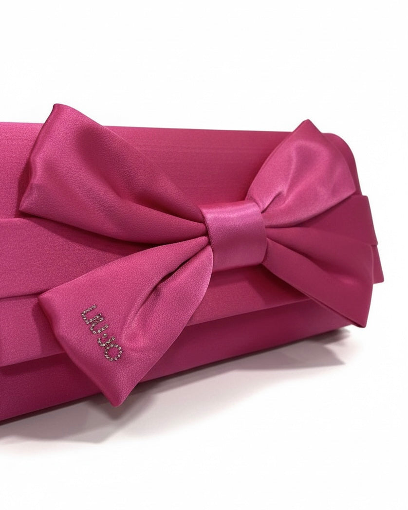 Borsa pochette fucsia Liu Jo in raso con grande fiocco frontale e piccolo logo metallico dorato, su sfondo bianco - dettaglio logo.