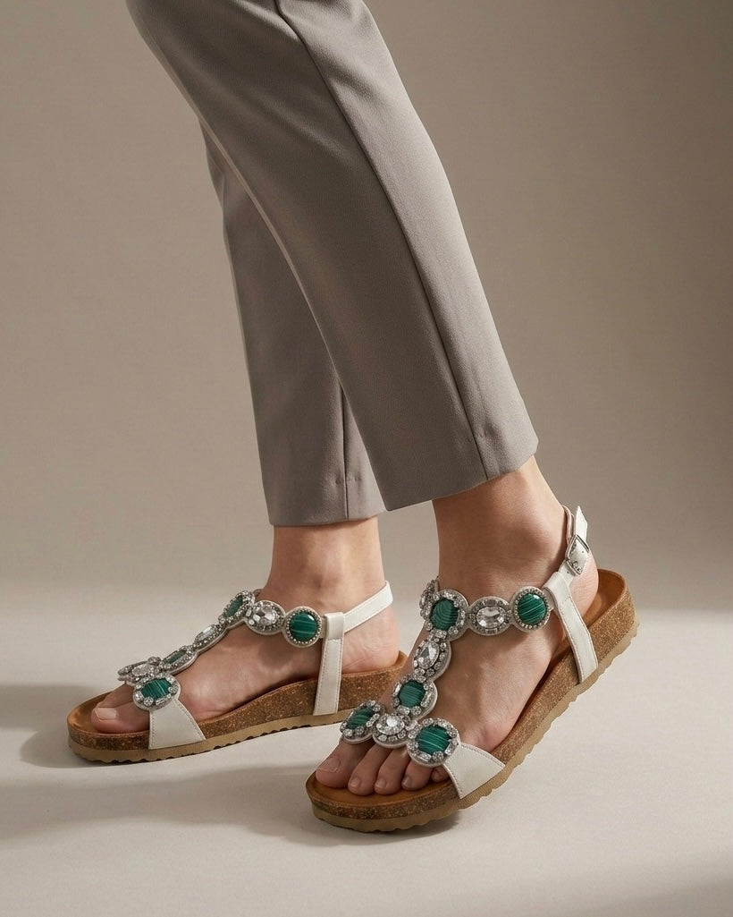 Sandali bassi da donna marca Igi&Co con grandi pietre circolari verdi screziate e cristalli luminosi, cinturino bianco e suola anatomica in sughero-indossati.