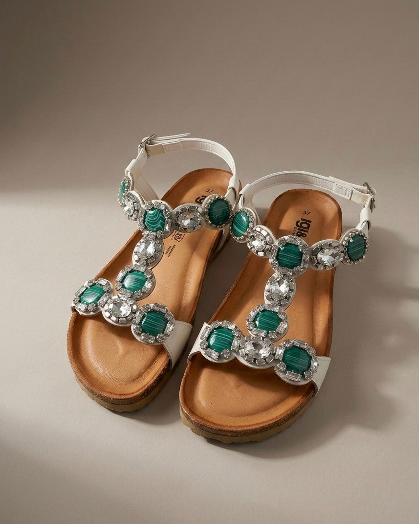 Sandali bassi da donna marca Igi&Co con grandi pietre circolari verdi screziate e cristalli luminosi, cinturino bianco e suola anatomica in sughero.