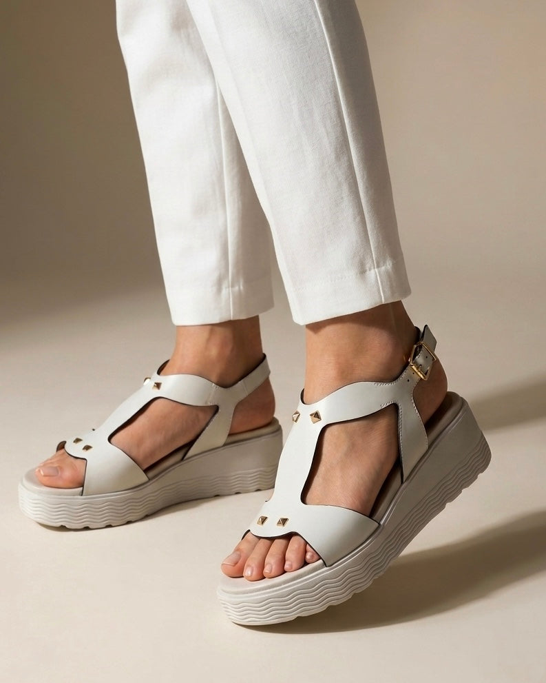 Sandali donna Stonefly in pelle bianca con suola platform alta, fascia centrale sagomata decorata con borchie dorate a piramide e cinturino alla caviglia-indossate.