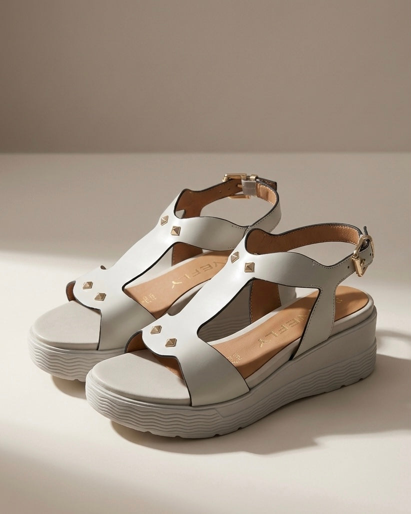 Sandali donna Stonefly in pelle bianca con suola platform alta, fascia centrale sagomata decorata con borchie dorate a piramide e cinturino alla caviglia.