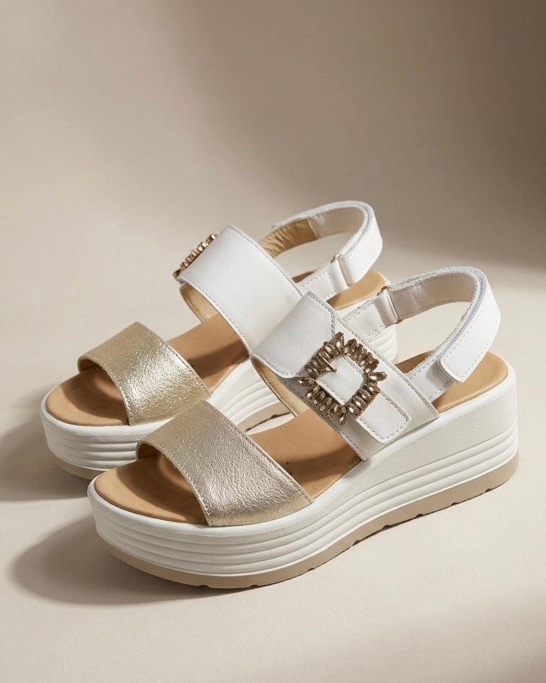 Sandali donna Igi&Co con zeppa platform bianca, fascia anteriore oro laminato e cinturino alla caviglia con fibbia rettangolare ricoperta di strass.