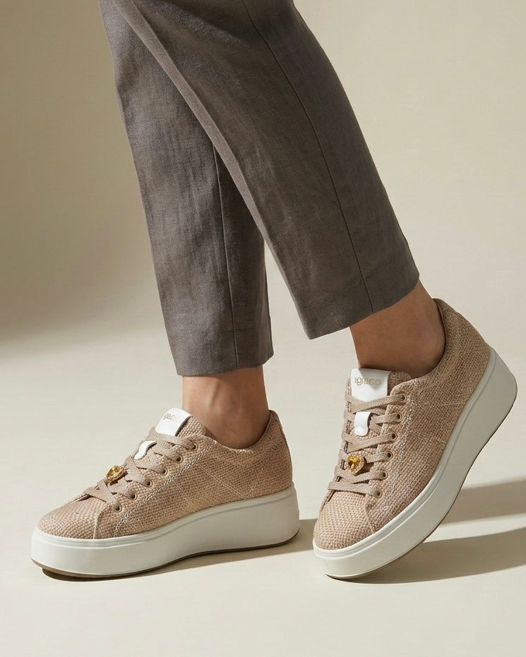 Sneakers da donna marca Igi&Co color beige panna con tomaia a texture intrecciata effetto rafia, cuori dorati metallizzati applicati sui lacci e suola platform bianca-indossate.