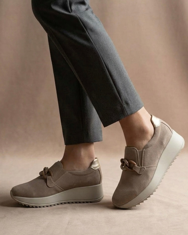 Sneakers slip-on da donna marca iMac in morbido camoscio color taupe/fango, con accessorio a catena dorata e strass, suola platform beige-indossate.