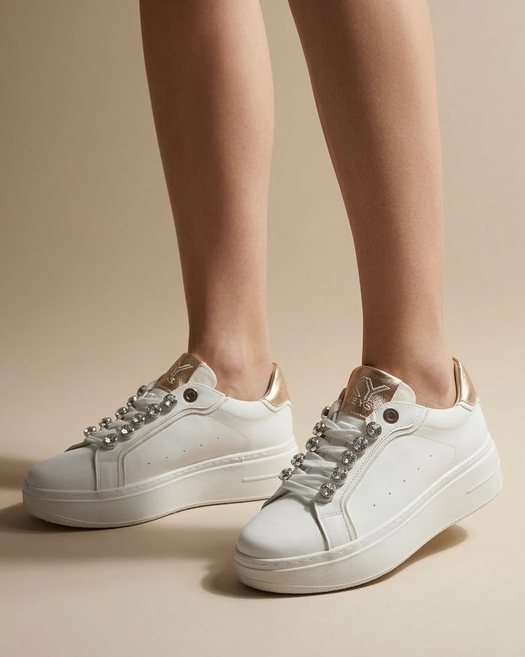 Sneakers donna bianche brand KEYS con grandi castoni gioiello sui lacci, linguetta e tallone oro rose lucido, suola platform panna-indossate.