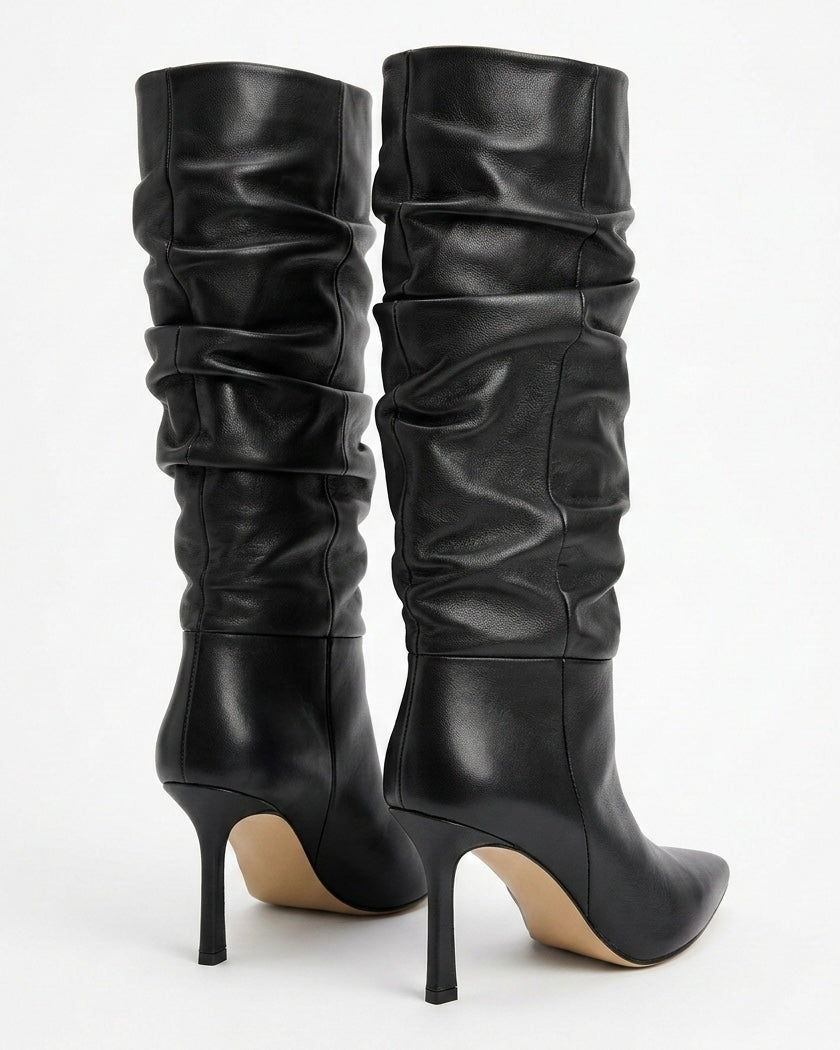 Stivali in pelle nera con gambale arricciato, punta affusolata e tacco alto a stiletto su sfondo bianco - retro tacco.