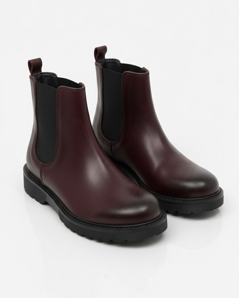 Stivaletti Chelsea bordeaux in pelle con inserto elastico nero, suola track a carrarmato e linguetta posteriore su sfondo neutro.