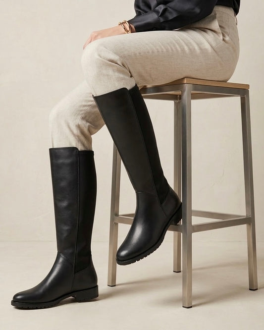 Stivali alti in pelle nera a tubo con suola piatta, punta arrotondata e design minimale-modella.